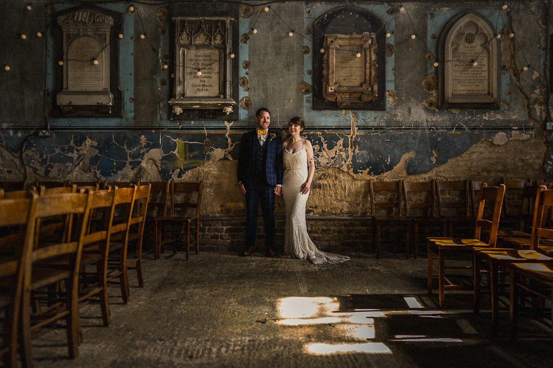 A wedding portrait of a couple against a blue, crumbling wall in a deserted venue in London
