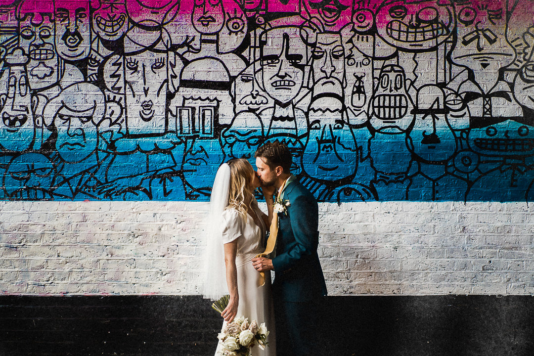 a wedding couple kiss in front of street art at Shoreditch Studios