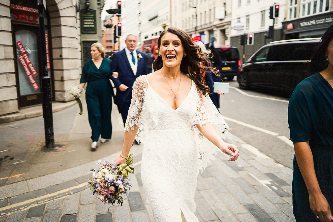an excited bride wearing grace loves lace walks to her wedding at st brides church in London